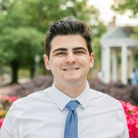 Portrait of Noah Cabanas in a white shirt and a blue tie.